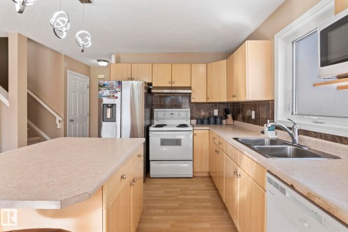Kitchen featuring light wood-finish cabinetry, light-colored countertops, stainless steel double basin sink, white built-in dishwasher, and wood-finish flooring - 92 4350 23 Street, Edmonton, AB - Indoor Photo Showing Kitchen With Double Sink