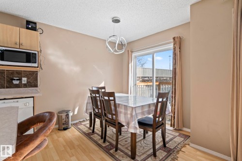 Open-concept dining area featuring wood-finish flooring, a contemporary chandelier, and a sliding glass door providing exterior access - 92 4350 23 Street, Edmonton, AB - Indoor Photo Showing Dining Room