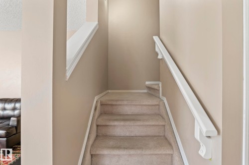Carpeted staircase featuring a white wall-mounted handrail, neutral wall paint, and white trim accents - 92 4350 23 Street, Edmonton, AB - Indoor Photo Showing Other Room