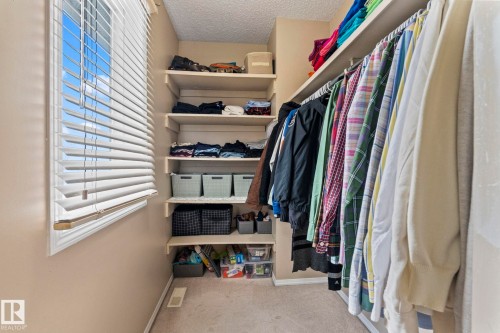 Walk-in closet featuring extensive built-in shelving, hanging rods, and a window with horizontal blinds - 92 4350 23 Street, Edmonton, AB - Indoor With Storage