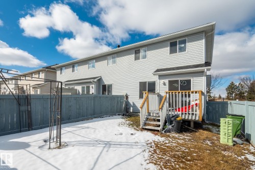 Rear exterior featuring light-colored siding, a private deck with wooden railing and stairs, and a fenced yard - 92 4350 23 Street, Edmonton, AB - Outdoor