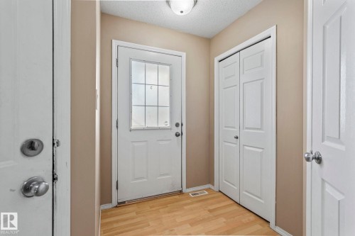 Entry foyer featuring wood-finish flooring, light beige wall paint, a white front door with multiple glass panes, a flush-mount ceiling light fixture, and white bi-fold closet doors - 92 4350 23 Street, Edmonton, AB - Indoor Photo Showing Other Room