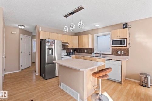 Kitchen featuring light wood-finish flooring, a central island with a light-toned countertop, and light wood cabinetry - 92 4350 23 Street, Edmonton, AB - Indoor Photo Showing Kitchen With Double Sink