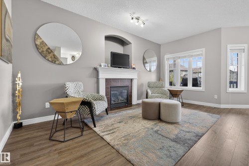 Living area featuring wood-finish flooring, a built-in fireplace with a white mantel and tile surround, an arched alcove, and multiple windows providing natural light - 2146 Austin Link Link, Edmonton, AB - Indoor Photo Showing Living Room With Fireplace