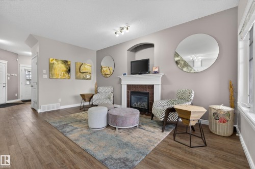 Living area featuring wood-finish flooring, light grey wall paint, and a tiled gas fireplace with a white mantel and an arched niche above - 2146 Austin Link Link, Edmonton, AB - Indoor Photo Showing Living Room With Fireplace