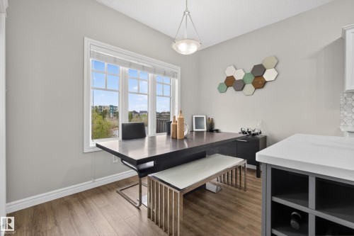 Dining area featuring a large window, pendant lighting, wood-finish flooring, and a kitchen island with built-in shelving - 2146 Austin Link Link, Edmonton, AB - Indoor Photo Showing Dining Room