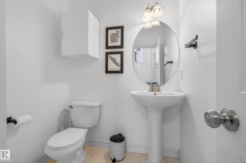 Bathroom featuring a pedestal sink, oval mirror, wall-mounted light fixture, and white wall cabinet - 2146 Austin Link Link, Edmonton, AB - Indoor Photo Showing Bathroom