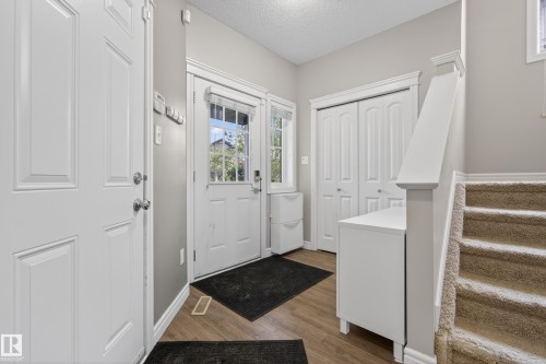 Entryway featuring wood-finish flooring, a white paneled entry door with sidelights, a double bifold closet, and a staircase with carpeted treads - 2146 Austin Link Link, Edmonton, AB - Indoor Photo Showing Other Room