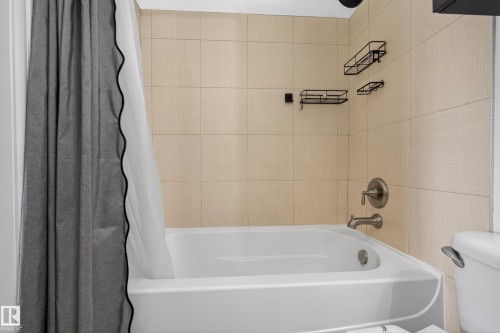 White bathtub and shower combination featuring neutral-toned rectangular wall tiles, brushed nickel fixtures, and wall-mounted storage racks - 2146 Austin Link Link, Edmonton, AB - Indoor Photo Showing Bathroom