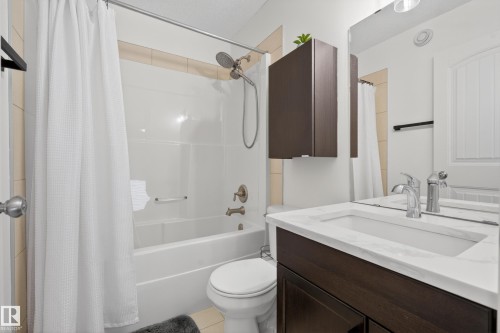 Bathroom featuring a shower-over-tub combination with a brushed bronze fixture, a dark wood-finish vanity with an integrated white sink, a large wall-mounted mirror, and a coordinating dark wood-finish wall cabinet - 2146 Austin Link Link, Edmonton, AB - Indoor Photo Showing Bathroom