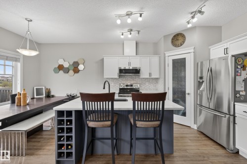 Kitchen featuring a central island with integrated wine storage, white cabinetry, stainless steel appliances, and wood-finish flooring - 2146 Austin Link Link, Edmonton, AB - Indoor