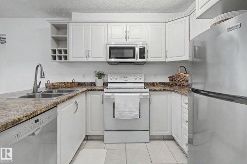 U-shaped kitchen featuring white cabinetry, stone-finish countertops, stainless steel sink with a gooseneck faucet, a built-in microwave, and tile flooring - 213 17404 64 Avenue, Edmonton, AB 