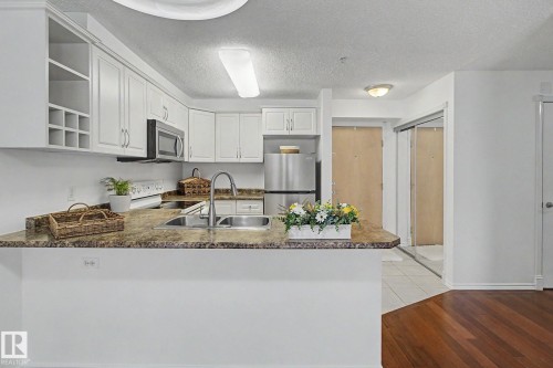 Kitchen featuring white cabinetry, stone-finish countertops, stainless steel appliances, and a double basin sink with a gooseneck faucet - 213 17404 64 Avenue, Edmonton, AB 