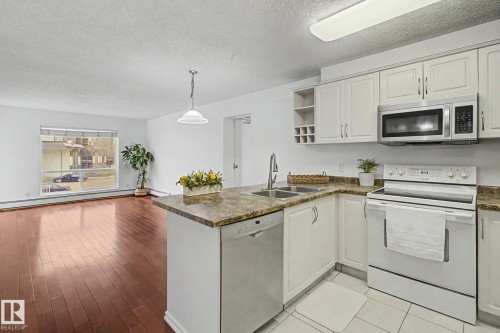 Kitchen featuring white cabinetry, stainless steel microwave, and a double basin sink - 213 17404 64 Avenue, Edmonton, AB 
