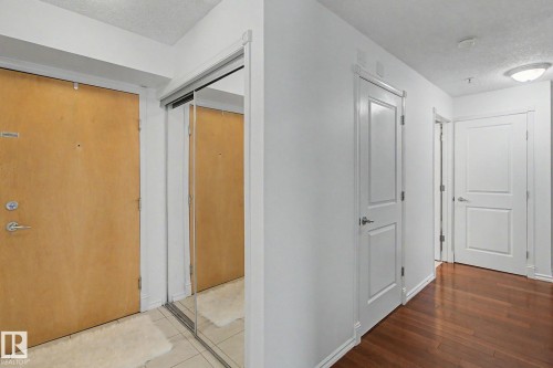 Entryway featuring a wood-panel door, mirrored closet doors, tile flooring, and a hallway with wood-finish flooring and white panel doors - 213 17404 64 Avenue, Edmonton, AB 