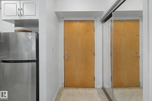 Entryway featuring a natural wood door, mirrored closet doors, and white walls - 213 17404 64 Avenue, Edmonton, AB 