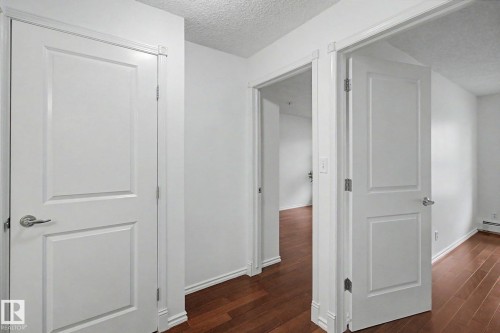 Hallway featuring wood-finish flooring, white paneled doors, and white trim - 213 17404 64 Avenue, Edmonton, AB 
