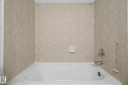 White alcove bathtub with light-toned square wall tiles, chrome fixtures, and a soap dish - 