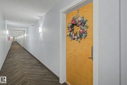 Building corridor featuring a light-toned entry door with a decorative wreath - 213 17404 64 Avenue, Edmonton, AB 