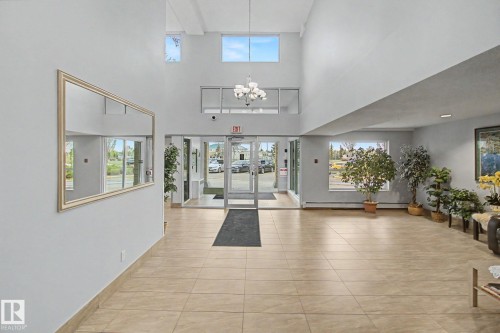 Bright common area featuring high ceilings, upper-level windows, and a multi-light chandelier - 213 17404 64 Avenue, Edmonton, AB 