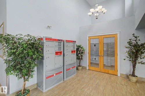 Building entryway featuring light-toned tile flooring and double glass-paneled doors with wood frames - 213 17404 64 Avenue, Edmonton, AB 