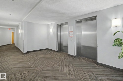 Two stainless steel elevators serving a hallway with geometric patterned carpet flooring - 213 17404 64 Avenue, Edmonton, AB 