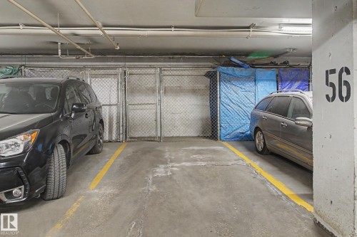 Designated parking space featuring a concrete floor, yellow painted lines, and overhead fluorescent lighting - 213 17404 64 Avenue, Edmonton, AB 