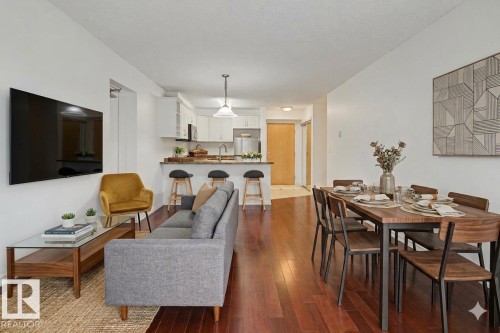 Open-concept living space featuring wood-finish flooring, a kitchen with white cabinetry and a breakfast bar, and a dedicated dining area - 213 17404 64 Avenue, Edmonton, AB 