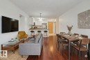 Open-concept living space featuring wood-finish flooring, a kitchen with white cabinetry and a breakfast bar, and a dedicated dining area - 213 17404 64 Avenue, Edmonton, AB 