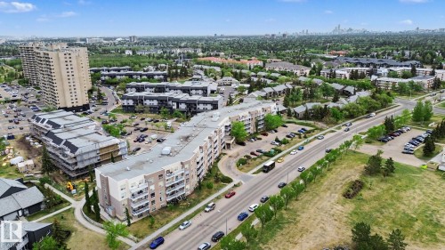 Aerial perspective showcasing the surrounding neighborhood, featuring multiple multi-story residential buildings, ample surface parking, mature trees, and nearby roadways - 213 17404 64 Avenue, Edmonton, AB 