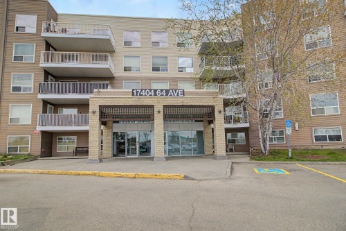 Multi-story residential building featuring a prominent stone facade entrance with a metal canopy, multiple private balconies with white railings, and a dedicated accessible parking space - 213 17404 64 Avenue, Edmonton, AB 