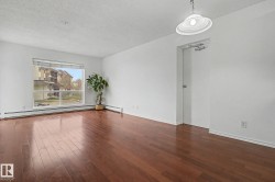 Spacious interior featuring wood-finish flooring, a large window, white walls, and a ceiling-mounted light fixture - 