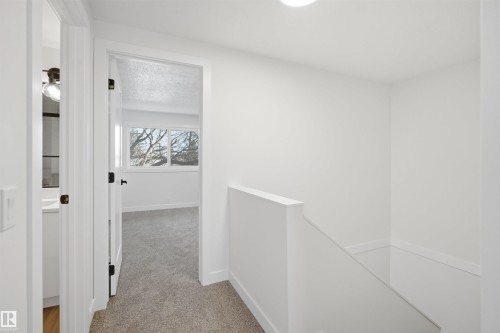 Carpeted hallway featuring a stairway with a half-wall railing, a room with a window, and a bathroom with a vanity and wood-finish flooring - 1706 37 Street, Edmonton, AB - Indoor Photo Showing Other Room