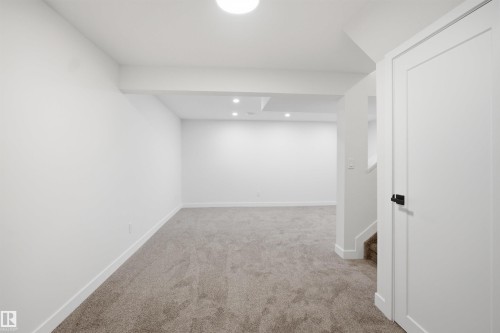 Expansive carpeted room featuring recessed lighting, a contemporary white door with matte black hardware, and crisp white baseboards - 1706 37 Street, Edmonton, AB - Indoor Photo Showing Other Room