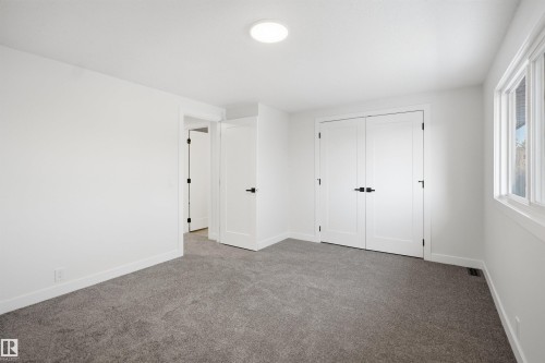 Spacious room featuring neutral carpeting, white walls, a large window with white trim, double panel doors with black hardware, and a circular flush-mount ceiling light - 1706 37 Street, Edmonton, AB - Indoor Photo Showing Other Room