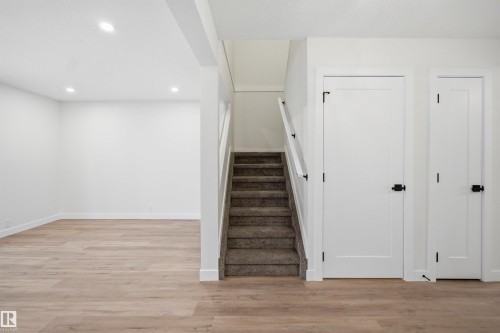 Recessed lighting illuminates an open area with wood-finish flooring, complemented by a carpeted staircase with a white handrail - 1706 37 Street, Edmonton, AB - Indoor Photo Showing Other Room