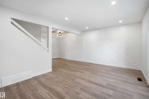 Spacious interior featuring wood-finish flooring, recessed lighting, and a decorative accent wall with diagonal paneling - 1706 37 Street, Edmonton, AB - Indoor Photo Showing Other Room
