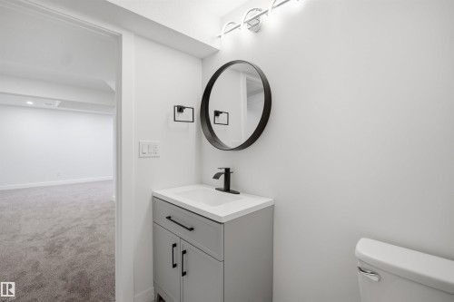 Contemporary bathroom featuring a vanity with a white countertop and matte black hardware, a round framed mirror, and modern wall-mounted lighting - 1706 37 Street, Edmonton, AB - Indoor Photo Showing Bathroom