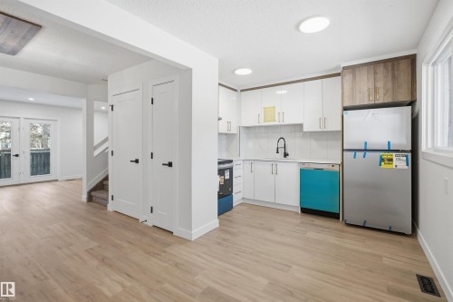 Modern kitchen with white cabinetry and wood-finish accent cabinets, stainless steel appliances, and a black faucet - 1706 37 Street, Edmonton, AB - Indoor Photo Showing Kitchen