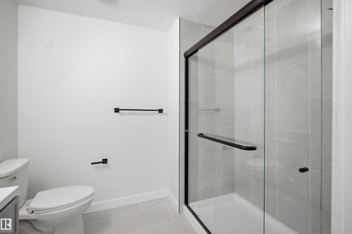 Contemporary bathroom featuring a frameless glass shower enclosure with matte black hardware, light-toned ceramic tile flooring, and a low-profile toilet - 1706 37 Street, Edmonton, AB - Indoor Photo Showing Bathroom