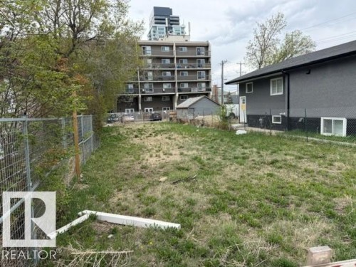 Expansive grassed area featuring a chain-link fence, mature trees, and a neighboring multi-story building - 9345 103A Avenue, Edmonton, AB 