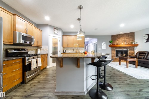 Kitchen featuring wood cabinetry, stainless steel appliances, speckled stone countertops, and a peninsula with pendant lighting - 2016 125 Street, Edmonton, AB - Indoor Photo Showing Kitchen With Fireplace With Upgraded Kitchen