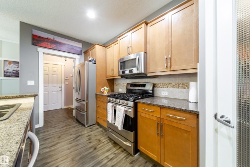 Kitchen featuring wood-finish flooring, granite-style countertops, stainless steel appliances, a tiled backsplash, and light wood cabinetry - 2016 125 Street, Edmonton, AB - Indoor Photo Showing Kitchen