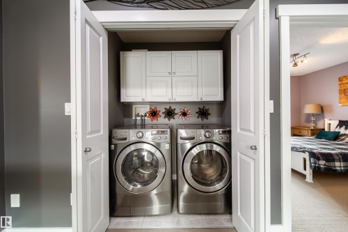 Dedicated laundry closet featuring a stacked washer and dryer, upper cabinetry, and a tile floor - 2016 125 Street, Edmonton, AB - Indoor Photo Showing Laundry Room