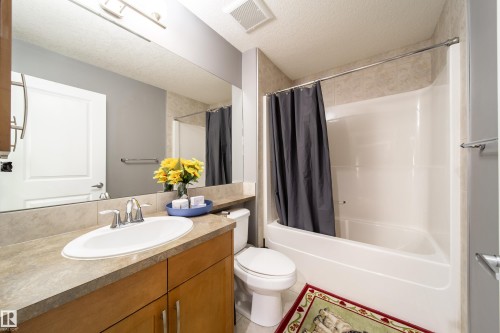 Bathroom featuring a vanity with a light wood-finish cabinet and a stone-look countertop, an oval undermount sink with a chrome faucet, a large wall-mounted mirror, and a full-size bathtub with a shower kit - 2016 125 Street, Edmonton, AB - Indoor Photo Showing Bathroom