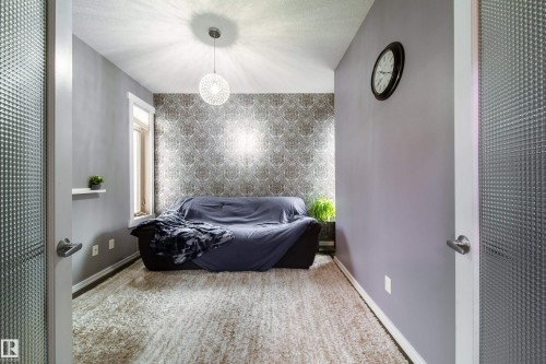 Textured glass door entry opens to a room featuring a patterned accent wall, a modern pendant light, a single window, and plush carpeting - 2016 125 Street, Edmonton, AB - Indoor Photo Showing Bedroom