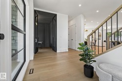 Light wood-finish flooring extends through an entryway featuring a black metal and glass front door - 