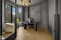 Dedicated interior space featuring light wood-finish flooring, dark paneled walls with detailed molding, and large window panels with dark framing - 