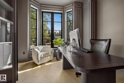 Bright room featuring a large bay window with dark-framed panes, light wood-finish flooring, built-in shelving with cabinetry, elegant wall molding, and a dark wood-finish desk - 13804 85 Avenue, Edmonton, AB - Indoor