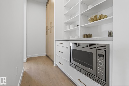 Built-in microwave with stainless steel trim, white cabinetry, integrated shelving, light wood-finish flooring, and additional tall cabinetry with gold-toned hardware - 13804 85 Avenue, Edmonton, AB - Indoor